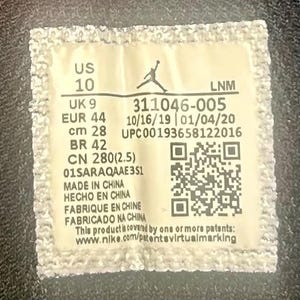 May include: A rectangular tag with text including "US 10", "UK 9", "EUR 44", and "cm 28". The tag also features a QR code and the text "MADE IN CHINA". The Nike logo is visible at the top.
