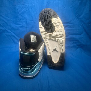 May include: Pair of black, white, and light blue Jordan sneakers. The sneakers have a black tongue and collar, with the word "Jordan" visible on the side. The soles are white and black, with the Jordan logo.