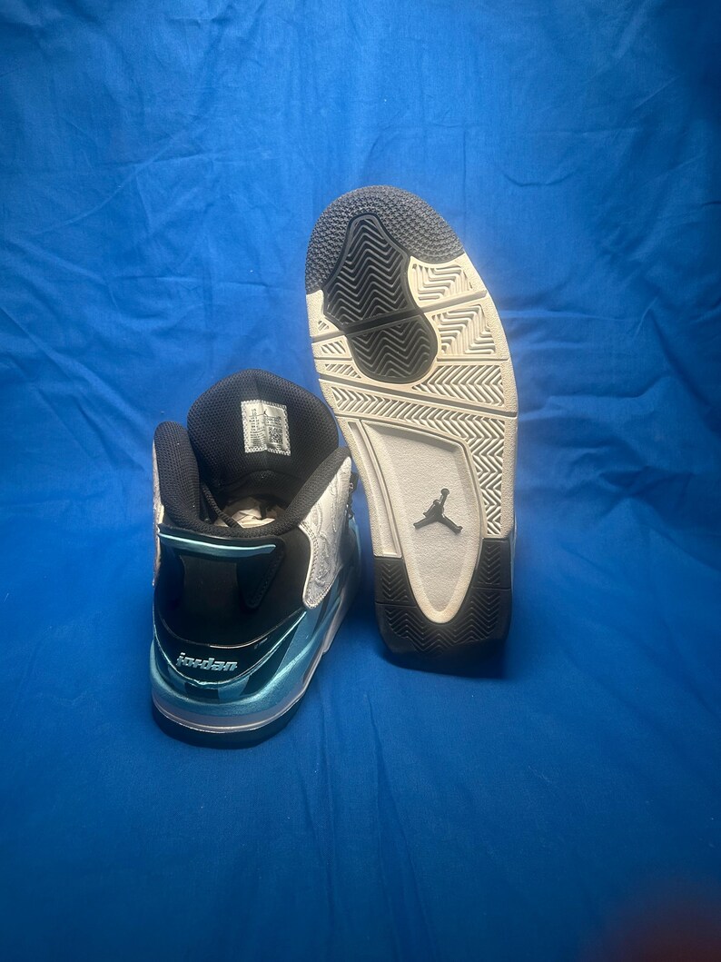 May include: Pair of black, white, and light blue Jordan sneakers. The sneakers have a black tongue and collar, with the word "Jordan" visible on the side. The soles are white and black, with the Jordan logo.