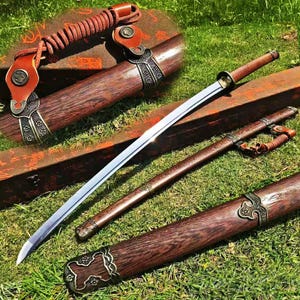 Pode incluir: Uma espada reta com lâmina de aço polido e cabo de madeira, acompanhada por uma bainha de madeira a condizer. A bainha apresenta veios de madeira escura, ferragens metálicas em tom de bronze e um cordão de couro castanho com detalhes.