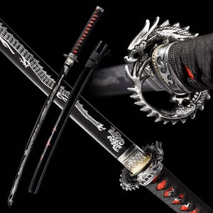 Op de afbeelding: Een zwart katana-zwaard met een zilveren, draakvormige tsuba-stootplaat en een handvat omwikkeld met zwart koord met rode accenten. De zwarte schede is versierd met een witte drakenillustratie en het lemmet toont gedetailleerde zilveren gravures.
