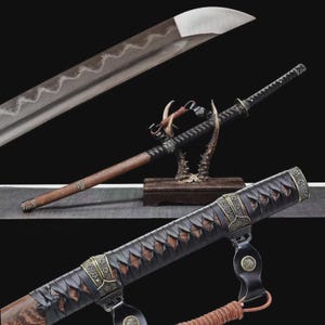 May include: A Japanese katana sword with a curved, silver blade and a wooden handle. The handle is wrapped in black fabric and features decorative metal accents. The sword is displayed on a wooden stand with a dark background.