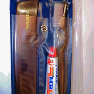 May include: A navy blue travel kit containing a brown comb, toothbrush, and toothpaste. The toothpaste tube is labelled "VARIG" and "MR Dental". The kit is sealed in a clear plastic bag. The comb and toothbrush are brown.