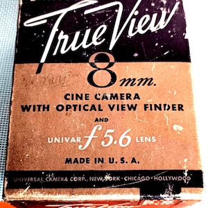 Puede incluir: Caja de cámara de cine Univex True View de 8 mm vintage. La caja es marrón y negra con texto blanco. El texto incluye "True View", "8mm", "Cine Camera", "Univar f5.6 Lens" y "Made in U.S.A."