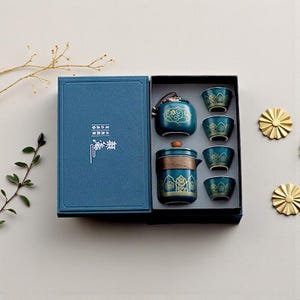 Könnte beinhalten: Ein türkisfarbenes Teeservice mit goldenen Akzenten, bestehend aus einer Teekanne, Teetassen und einem kleinen Behälter, präsentiert in einer blauen Box. Das Set weist verzierte florale Designs auf.