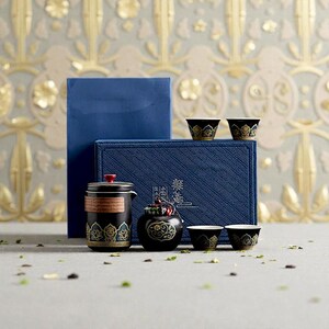 Peut inclure: Un service &agrave; th&eacute; noir et dor&eacute; avec une th&eacute;i&egrave;re, des tasses et un petit r&eacute;cipient assortis. L'ensemble &agrave; th&eacute; est pr&eacute;sent&eacute; devant une bo&icirc;te bleue. L'ensemble &agrave; th&eacute; pr&eacute;sente des motifs floraux dor&eacute;s. Le fond est un motif floral dor&eacute; et gris.