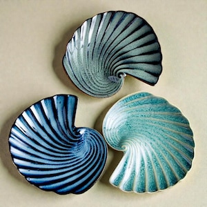 Könnte beinhalten: Drei Keramikplatten in Form einer Nautilusmuschel. Die Platten sind in Blau- und Türkistönen gehalten und weisen ein Spiralmuster auf. Die Platten haben eine strukturierte Oberfläche und einen braunen Rand. Die Platten sind dekorativ und zum Servieren geeignet.