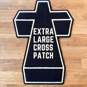 Peut inclure: Un écusson en forme de croix, noir et extra large, avec un contour blanc et l'inscription "EXTRA LARGE CROSS PATCH" en blanc. L'écusson est posé sur une surface en bois.