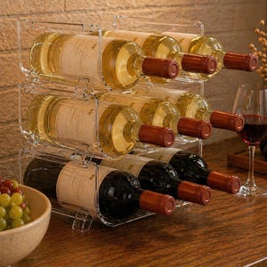 May include: A clear acrylic wine rack holding several bottles of wine. The rack is stacked with three levels, each holding multiple bottles. The wine bottles are filled with white and red wine, with brown corks and labels.