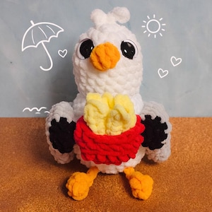 Könnte beinhalten: Ein handgefertigter weißer Häkelvogel mit schwarzen Akzenten, großen schwarzen Augen und einem orangefarbenen Schnabel und Füßen. Der Vogel hält einen roten Korb mit gelben Pommes Frites. Der Hintergrund ist hellblau mit einer Zeichnung eines Regenschirms, einer Sonne und Herzen.