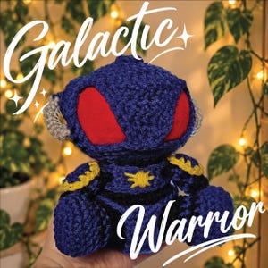 Può includere: Un peluche lavorato all'uncinetto blu scuro con grandi occhi in feltro rosso, dettagli laterali grigi e decorazioni gialle sul petto e sulle spalle. Il testo "Galactic Warrior" è sovrapposto in bianco sull'immagine.