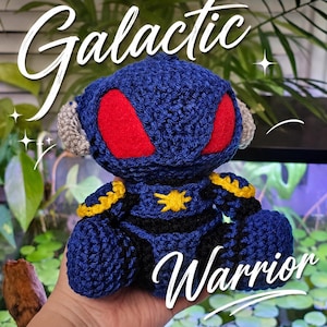 May include: A handmade blue crochet Galactic Warrior doll with red eye accents, yellow trim, and a star emblem. The doll has grey ear details and the words "Galactic" and "Warrior" in white script.