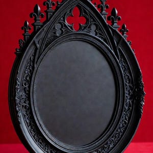 May include: A black gothic-style decorative frame with an oval center and ornate detailing. The frame features a pointed arch design with fleur-de-lis accents and a quatrefoil opening. The background is a solid red.