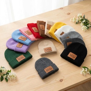Pode incluir: Uma coleção de gorros de malha em várias cores, incluindo vermelho, azul, roxo, verde, amarelo, branco, cinza, marrom e bege. Cada gorro apresenta um emblema retangular de couro marrom com o nome Milo gravado no centro.