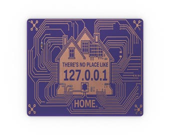 Op de afbeelding: Een rechthoekig paars metalen bord met een koperkleurig printplaatpatroon. In het midden bevat een huisomtrek de tekst "THERE'S NO PLACE LIKE 127.0.0.1 HOME." met koperen lijnen die naar de hoeken van het bord uitlopen.