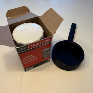 May include: A new Motorcraft oil filter in its cardboard box, with a black oil filter wrench. The box is red and white with the Ford logo and the words "Oil Filter". The filter is white.