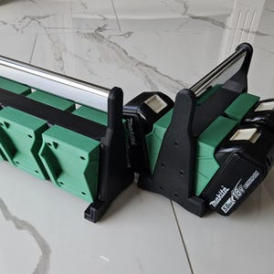 Puede incluir: Un organizador de baterías negro y verde con un asa plateada. El organizador tiene múltiples ranuras para baterías y presenta el logotipo de Makita. Las baterías están etiquetadas como 18V.