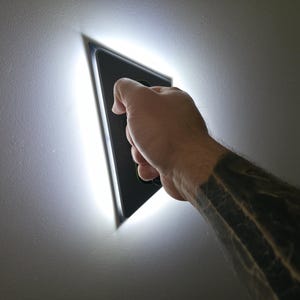 Könnte beinhalten: Eine dreieckige schwarze Glättkelle mit integriertem LED-Lichtstreifen entlang des Umfangs. Das Werkzeug hat einen dunklen Griff und strahlt ein helles weißes Licht von den Kanten aus, um Oberflächen während des Glättens zu beleuchten.