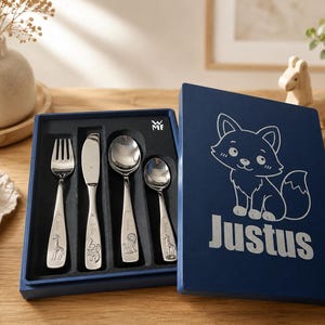 Könnte beinhalten: Ein vierteiliges Kinderbesteck-Set aus Edelstahl mit Gabel, Messer und zwei Löffeln in einer dunkelblauen Box. Der Deckel zeigt eine weiße Strichzeichnung eines Fuchses und den Namen Justus. Jeder Besteckgriff ist mit einem Tier graviert.