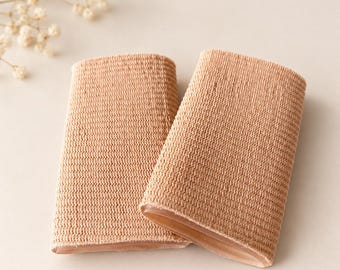 May include: Two beige finger sleeves made of a flexible, knit fabric. Each sleeve features a textured, woven exterior surface and a smooth, semi-transparent gel-like lining visible at the open end, designed for finger protection.