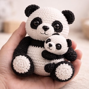 May include: A crocheted panda bear and its smaller replica, both in black and white. The larger panda has black ears, eyes, arms, and legs, with a white face and body. The smaller panda is held by the larger one.