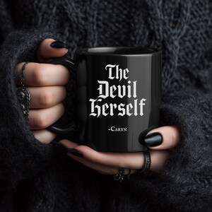 Puede incluir: Una taza de cerámica blanca con un asa negra y el texto "But First, Coffee" en negro y negrita. La taza está sobre una superficie de madera. La taza mide aproximadamente 10 cm de alto.