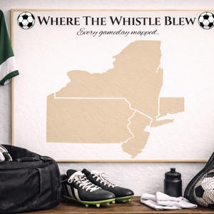 Puede incluir: Un mapa enmarcado del estado de Nueva York con el texto "Where The Whistle Blew" y balones de fútbol. Una camiseta verde con el número 9 cuelga de la pared. Equipamiento de fútbol, incluyendo una bolsa de deporte, tacos y balones, están sobre una superficie de madera.