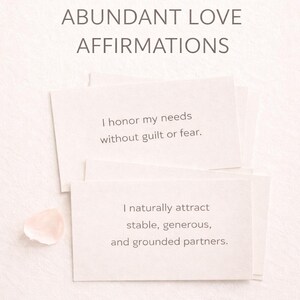 May include: A soft, neutral-toned image features stacked affirmation cards with the text "ABUNDANT LOVE AFFIRMATIONS." The cards include phrases like "I honor my needs" and "I naturally attract stable partners." The words "INSTANT DIGITAL DOWNLOAD" are also visible.