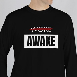 May include: Black long-sleeve shirt with the word "WOKE" crossed out in red above the word "AWAKE" in a white rectangle. The shirt is a solid black color.