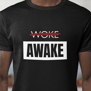 May include: Black t-shirt with the word "WOKE" crossed out in red above the word "AWAKE" in a white rectangle. The shirt is made of a soft material and has short sleeves.