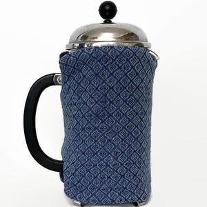 May include: A stainless steel French press coffee maker with a black handle and a blue patterned cozy. The cozy is made of fabric with a diamond pattern. The coffee maker is designed for brewing coffee.