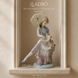 May include: A Lladro porcelain figurine titled Picture Perfect #7612, featuring a seated figure in a blue top and white skirt with pink lace trim, holding a white parasol with a gold handle, accompanied by a small dog, measuring 8.75 inches by 5.5 inches.