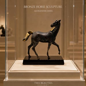 May include: A dark bronze horse sculpture by Alexsander Danel, featuring gold-toned accents on the mane, tail, and hooves. The horse stands on a rectangular black base, with the text BRONZE HORSE SCULPTURE and ALEXSANDER DANEL visible above.