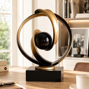 Peut inclure: Une sculpture décorative composée d'une sphère centrale noire brillante entourée de deux anneaux circulaires entrelacés, l'un au fini noir mat et l'autre en or métallique, le tout monté sur une base rectangulaire noire solide.