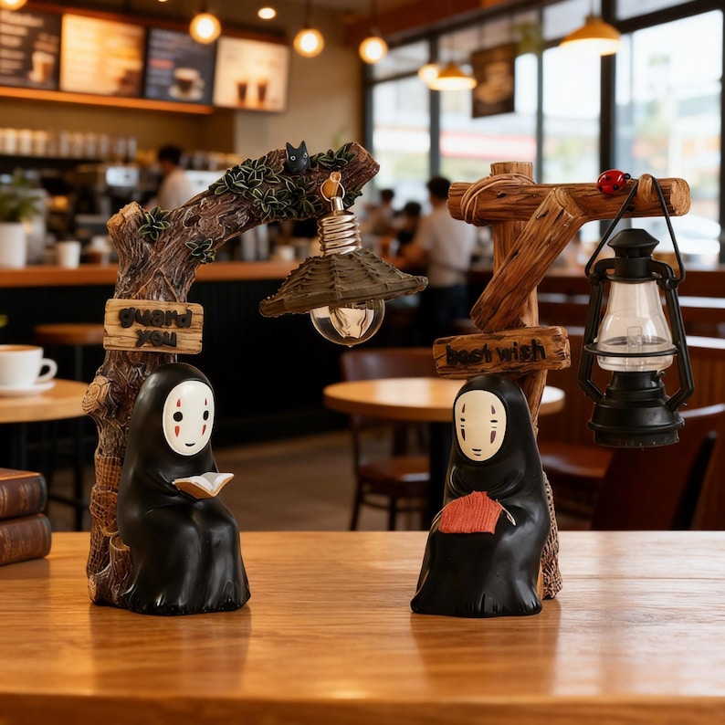 May include: Two decorative figurines featuring characters from Spirited Away. One holds a book and the other a fan. The figurines are black with white masks and are set on a wooden base. One has a light bulb and the other a lantern. The text on the base reads "guard you" and "best wish".