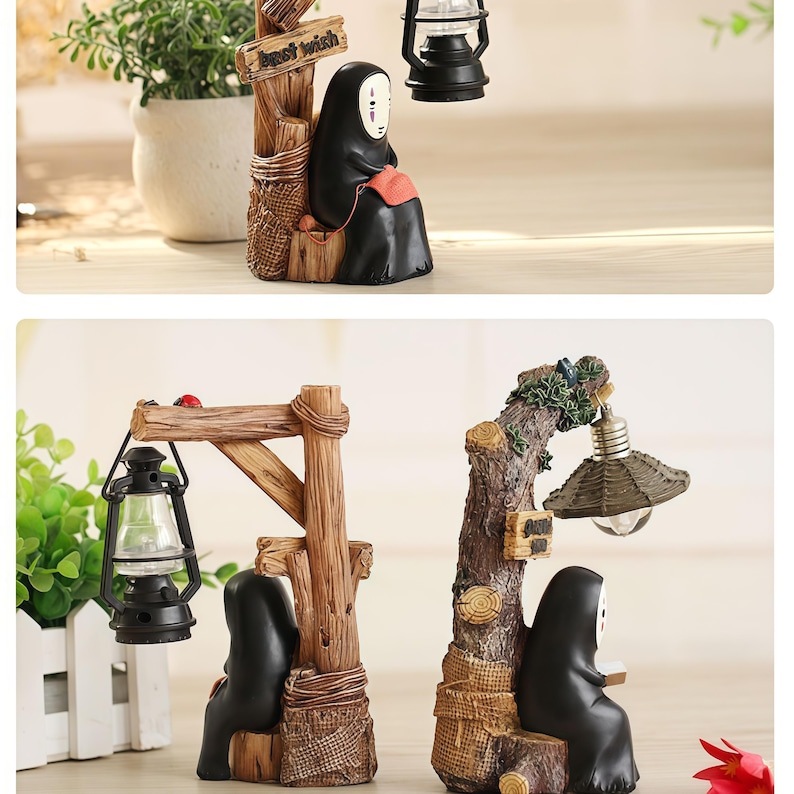 May include: Two decorative figurines featuring a character in a black robe with a white mask. One figurine has a lantern hanging from a wooden structure, the other has a lamp. The figurines are set on a wooden base.