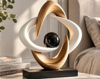 May include: A decorative sculpture featuring two interlocking curved forms, one with a light wood grain finish and one in matte white, surrounding a central glossy black sphere. The entire structure is mounted on a rectangular black base.