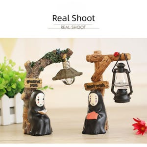 May include: Two decorative figurines featuring characters from a popular animated film. One holds a book under a lamp, the other knits under a lantern. The text "Real Shoot" is at the top.