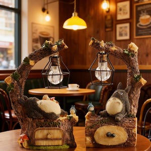 May include: Two decorative lamps with a tree trunk design, featuring a clear light bulb in a black cage. The lamps have a cartoon character on top of the trunk. The lamps are brown, with green and yellow accents.