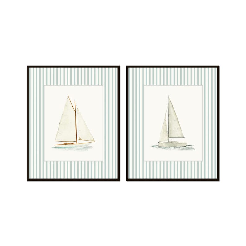 May include: Two framed watercolor prints of sailboats. Each print features a white sailboat with a beige sail on a light blue and white striped background. The frames are black.