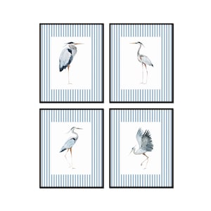 May include: Set of four framed prints featuring watercolor illustrations of blue herons on a blue and white striped background.