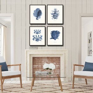 Op de afbeelding: Vier ingelijste prints van blauwe en witte illustraties van koraal en zeewier. De prints zijn gerangschikt in een rasterpatroon op een witte bakstenen open haard.