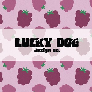 May include: A repeating pattern of dark purple berries with green stems on a light pink background. The text "LUCKY DOG design co." is displayed in black, bold font on a white banner.