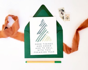May include: A green envelope with a white card inside. The card has a stylized blue and green tree design and the text "Good Tidings and Cheer and to hell with this freaking year".