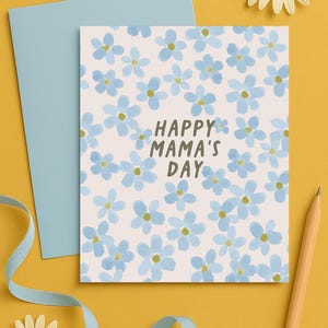 May include: A light blue card with a white background and a pattern of blue flowers. The text "Happy Mama's Day" is written in brown letters on the card.