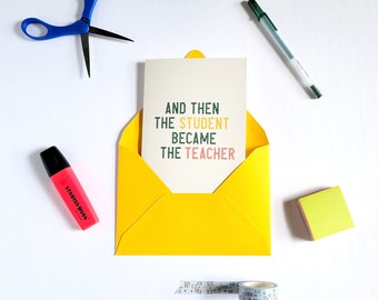 May include: A greeting card in a yellow envelope with the text "AND THEN THE STUDENT BECAME THE TEACHER". The image also includes a pink highlighter, blue scissors, a green pen, a small stack of sticky notes, and decorative tape.