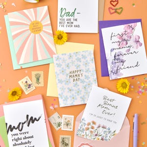 May include: A selection of greeting cards with different designs and messages for Mother's Day. The cards feature floral patterns, handwritten text, and colourful backgrounds. Some of the messages include "Happy Mama's Day", "Best Bonus Mom Ever!" and "First my mama, forever my friend".