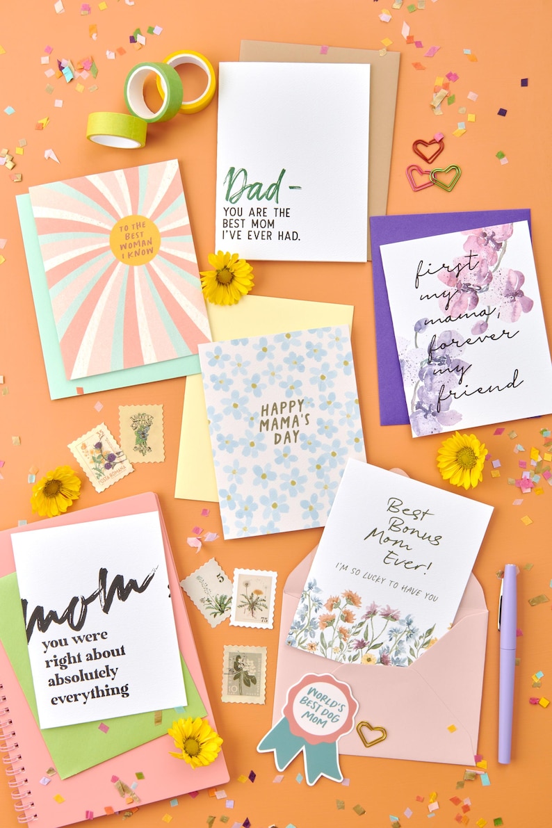 May include: A selection of greeting cards with different designs and messages for Mother's Day. The cards feature floral patterns, handwritten text, and colourful backgrounds. Some of the messages include "Happy Mama's Day", "Best Bonus Mom Ever!" and "First my mama, forever my friend".