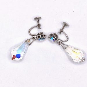 May include: A pair of vintage screw-back earrings. Each earring features a silver-tone metal setting with a faceted, iridescent crystal teardrop pendant. The crystals reflect a rainbow of colors, adding sparkle and elegance.