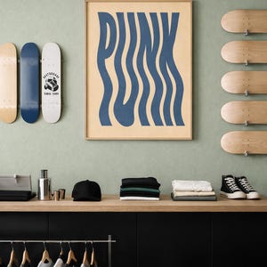 Op de afbeelding: Een kamer met een lichtgroene muur met een ingelijste poster met het woord "PUNK" in blauwe golvende letters. Er zijn skateboards, kleding en accessoires, waaronder een zwarte pet en high-top sneakers.